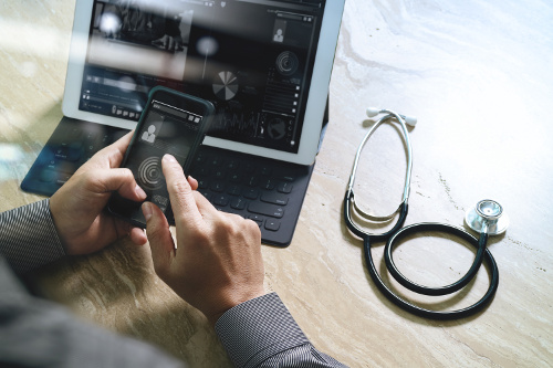 Doctor using cellphone in front of a tablet next to a stethoscope